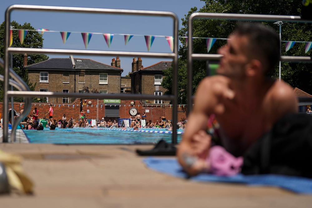 People sunbathe by an outdoor swimming pool in London on Tuesday (AP)