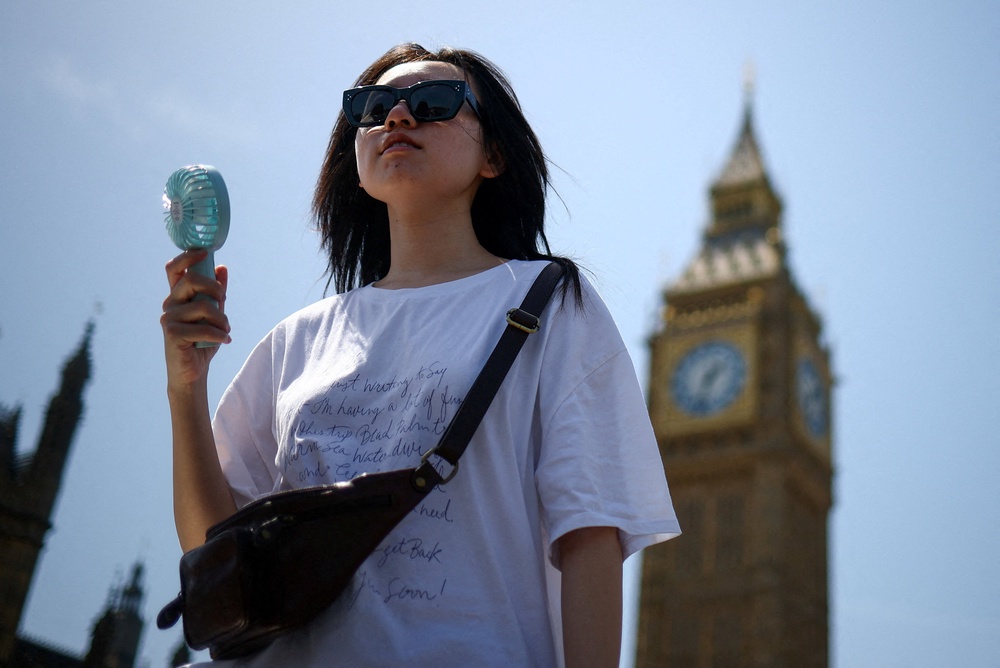 A woman uses a fan as she walks near the Houses of Parliament, amid hot weather in London (Reuters)