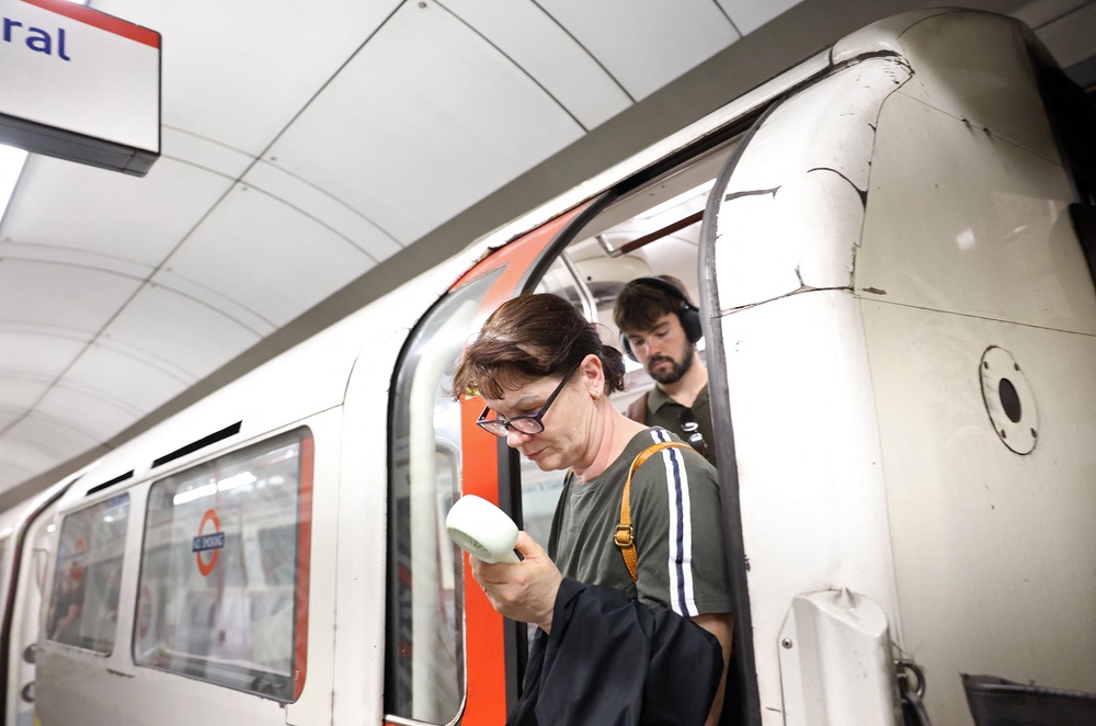 A commuter uses a fan in an attempt to cool down, as they exit a London Underground tube carriage, in London on 23 June 2026 (AFP/Getty)