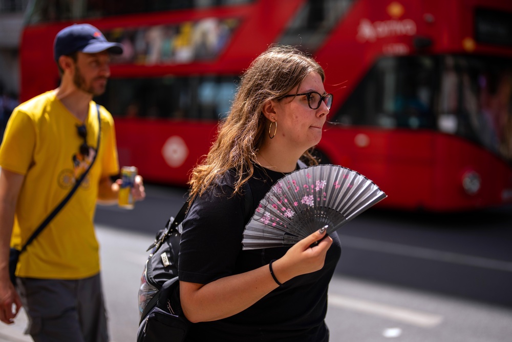 A woman uses a fan to cool herself as she walks through central London in the hot weather (Getty)