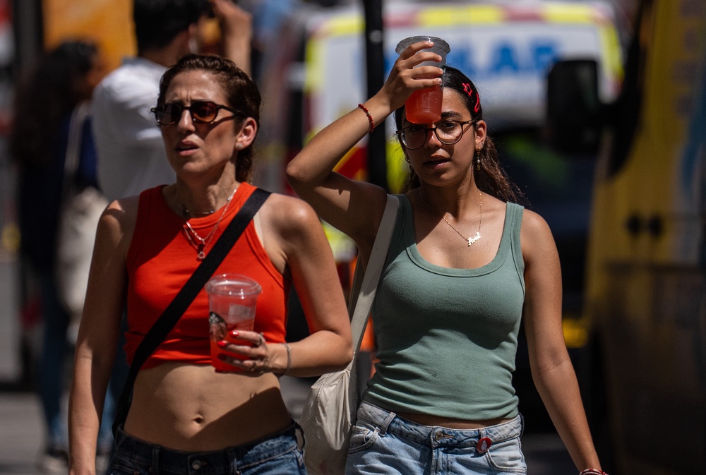 A woman cools her head with an iced drink as she walks through central London (Getty)