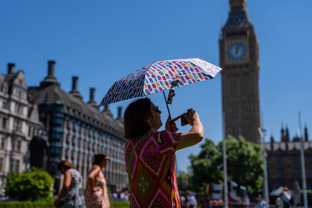A woman shelters from the sun under an umbrella as she takes photographs in Parliament Square (Getty)