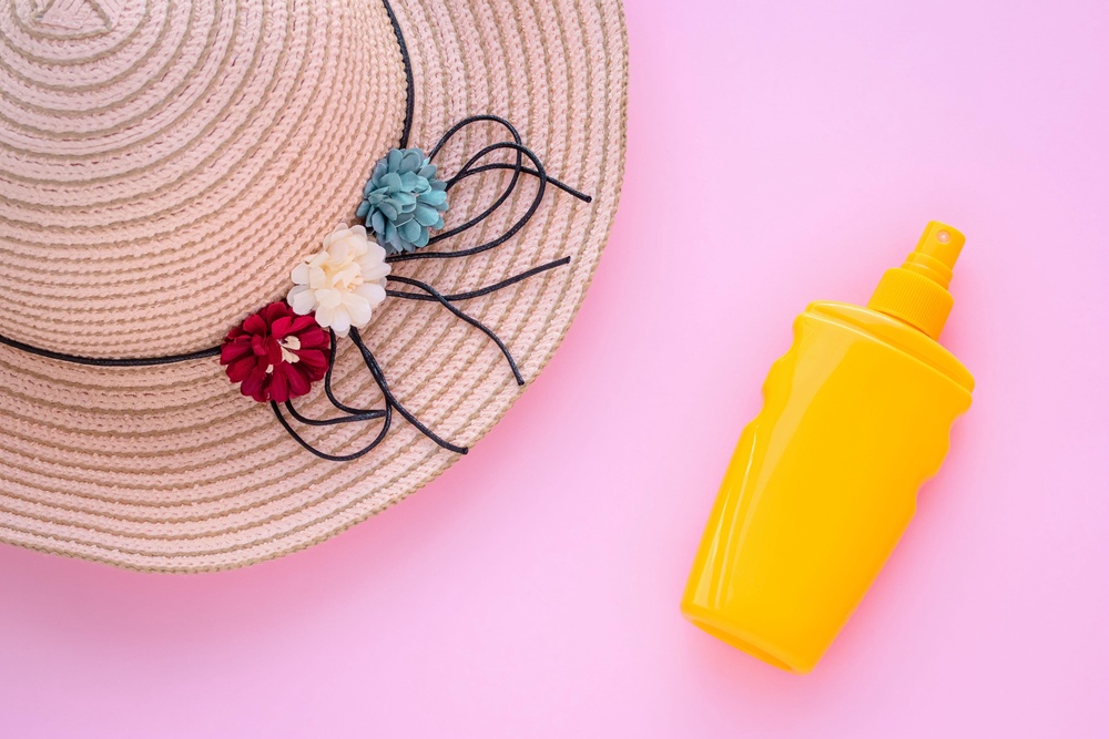 Wicker hat and sunscreen in bottle against pink backdrop (Alamy/PA)