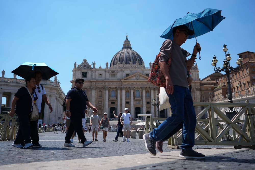 People shade from the sun under umbrellas as they walk through St. Peter's Square at the Vatican (AP)