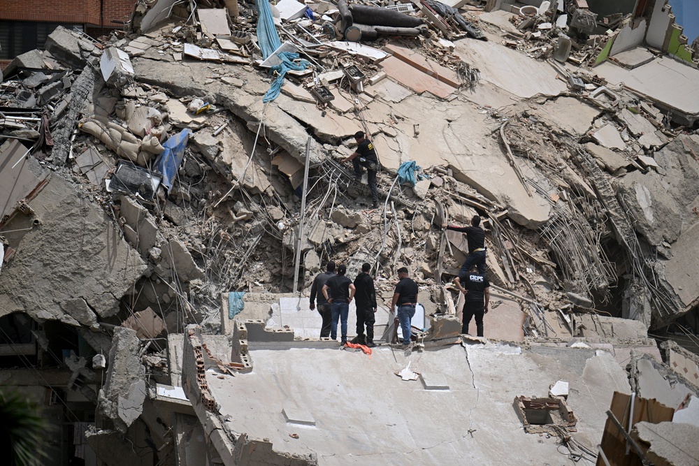 Rescue workers stand on the slab of a collapsed building amid twisted rebar and debris during search operations following an earthquake in Catia La Mar, La Guaira state, about 30 km northwest of Caracas (AFP/Getty)