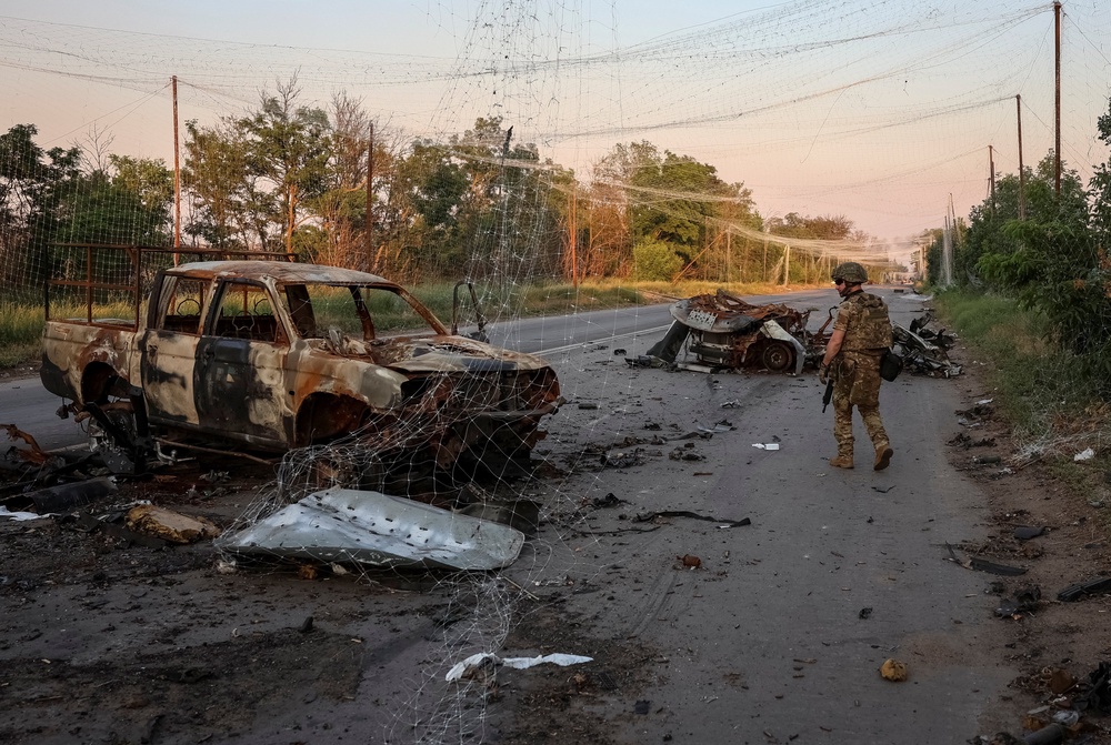 Ukrainian soldiers walks along a road near anti-drone nets and destroyed military vehicles as he takes part in a mission to protect a road from Russian drones between frontline towns of Druzhkivka and Kostiantynivka, on 24 June (Reuters)