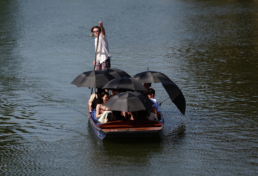 People shade under umbrellas as they take a punt tour along the River Cam in Cambridge (PA) (PA Wire)