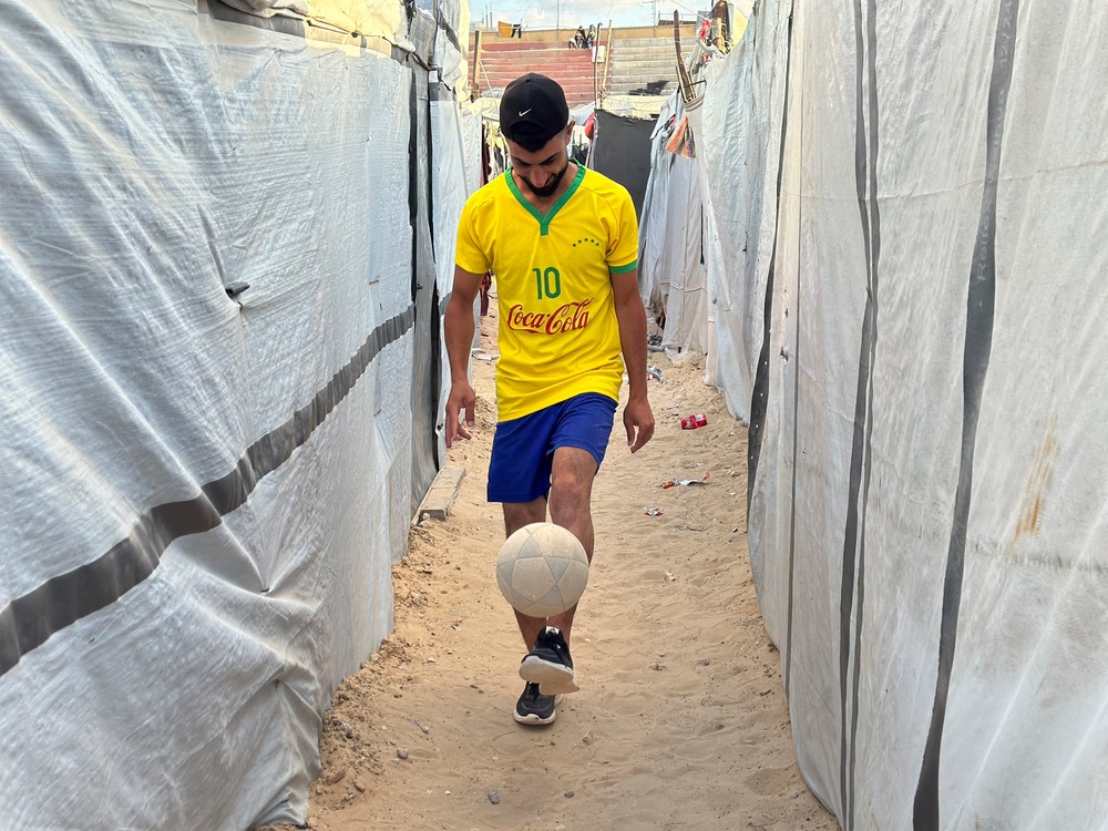 A Palestinian football player moves with a ball between tents sheltering displaced Palestinians at the war-damaged Khan Yunis Services Club in Khan Yunis, Gaza Strip, on June 22, 2026 The Khan Yunis Services Club, once one of southern Gaza's main sports clubs, has been turned into a shelter for displaced families after sustaining major damage during the war. (AFP/Getty)