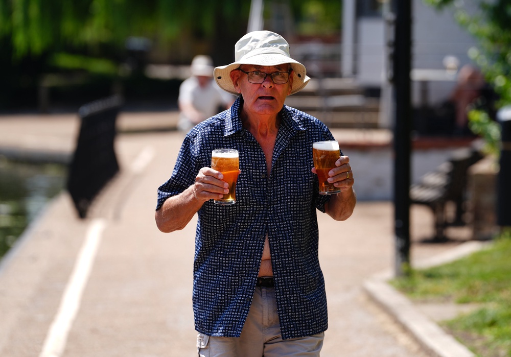 A man holds two pints as he walks next to the River Great Ouse in Ely during the last heatwave (PA)