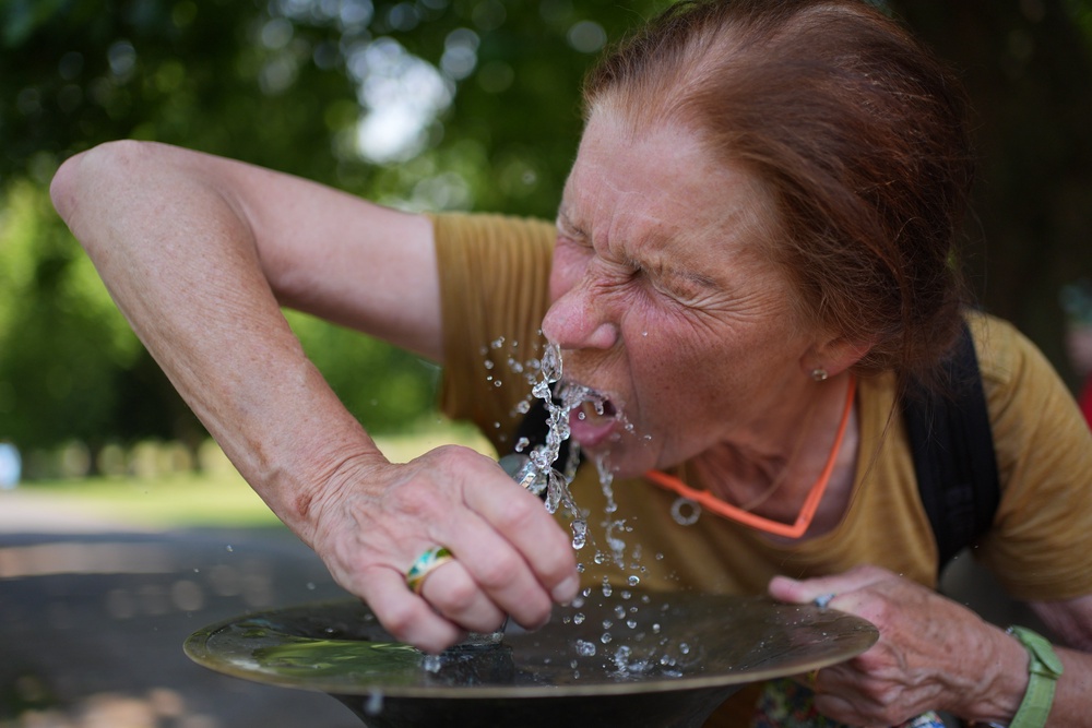 A woman drinks from a drinking fountain in Greenwich Park, London (PA)
