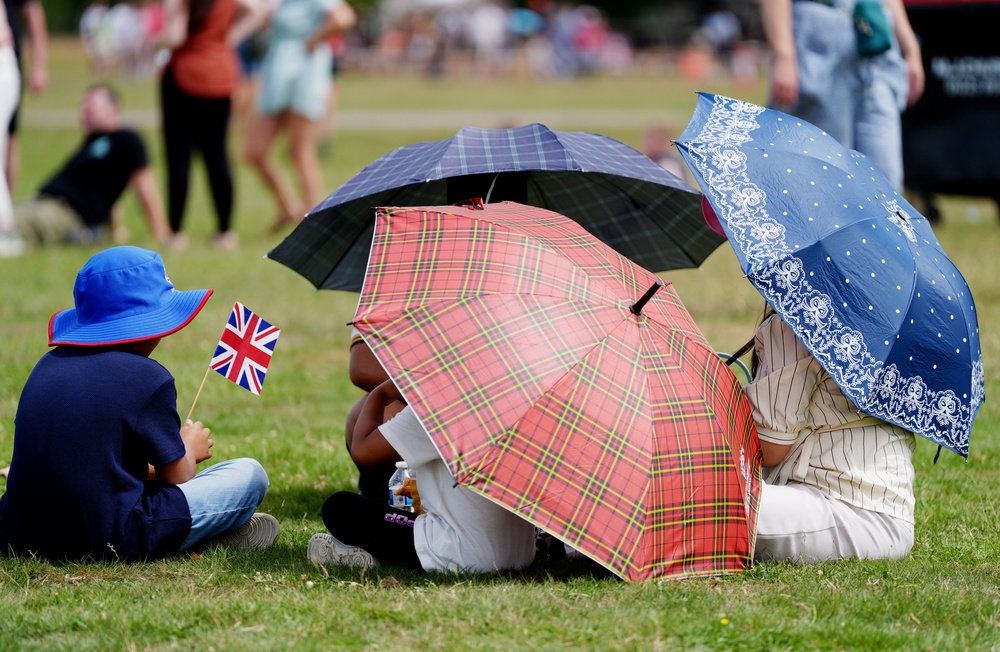A family shelter under umbrellas during an Armed Forces Day event in Aldershot, Hampshire (PA)