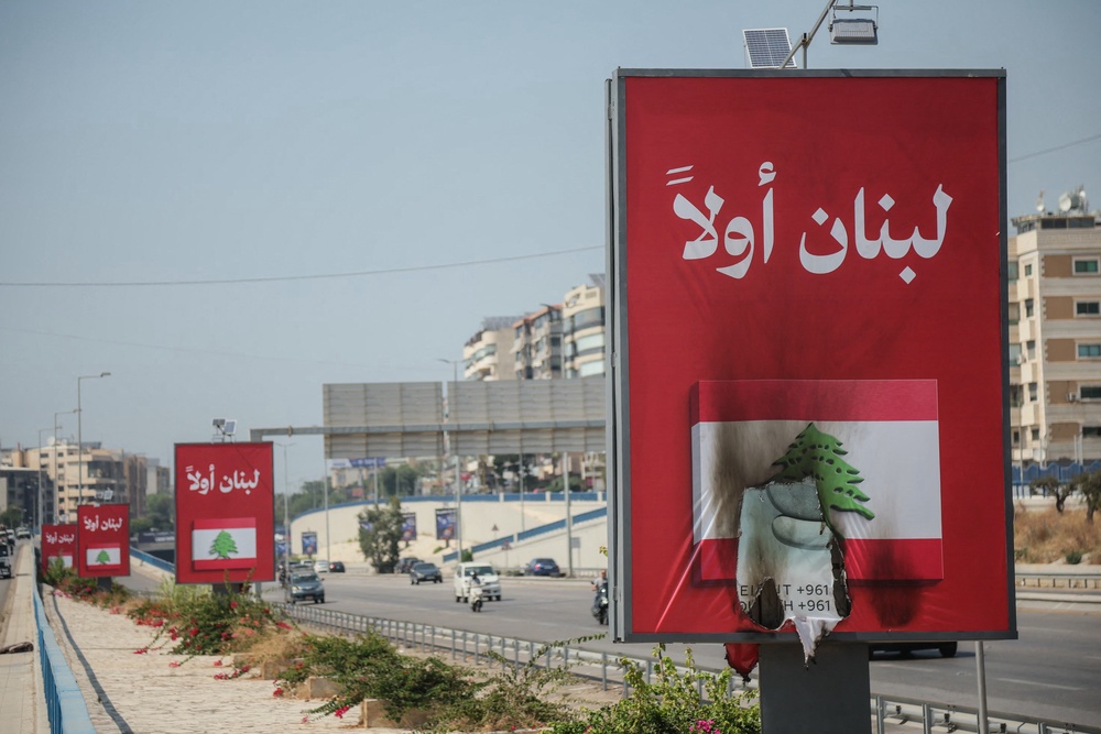 Vehicles drive past billboards that read in Arabic, Lebanon first, one of which has been set on fire along Beirut's airport road near Tehran-backed Hezbollah's stronghold, amidst tensions following Lebanon's framework agreement with Israel on 28 June 2026 (AFP/Getty)
