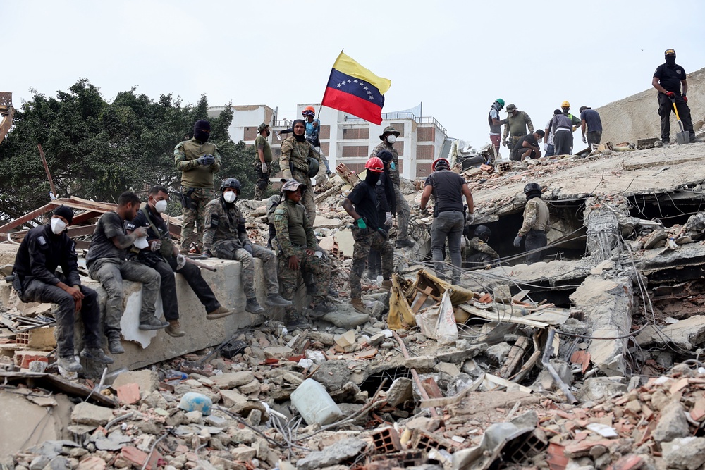 Rescuers search for victims at a collapsed building as one raises a Venezuelan flag following a magnitude 7.2 earthquake that struck Venezuela and other regions in the Caribbean (Getty)