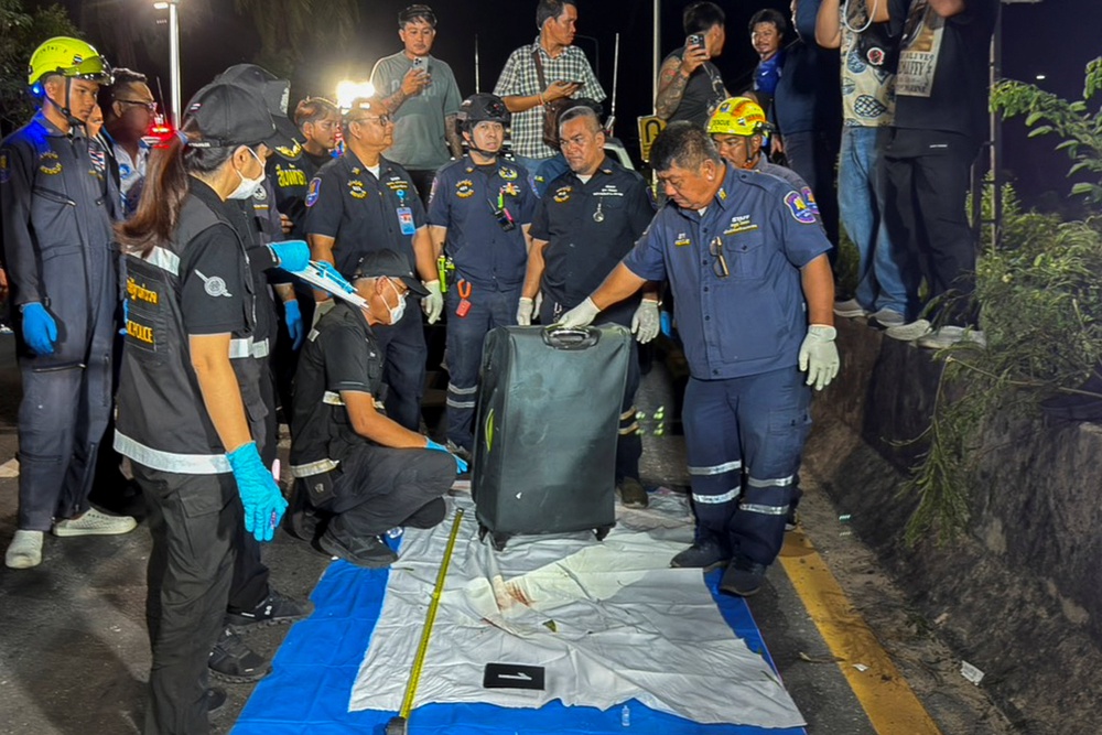 Rescue workers and forensic technicians with a suitcase, in which police later found the body of a 17-year-old Thai girl, for examination, after it was recovered from a grassy area near a railway track in Pattaya City, Thailand (Reuters)