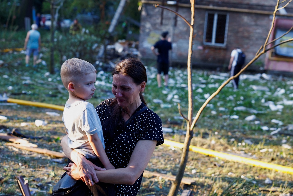 A woman holds a child near an apartment building damaged in overnight Russian strikes in Kyiv, Ukraine, on 2 July 2026 (Reuters)