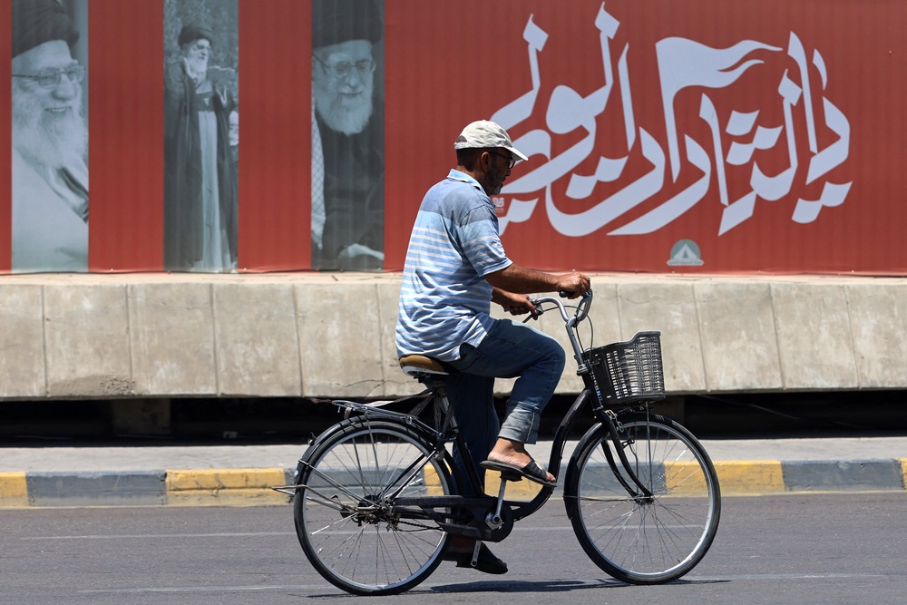 A cyclist rides past a billboard bearing pictures of Iran's late supreme leader Ayatollah Ali Khamenei, along a street in Baghdad on July 2, 2026, ahead of his funeral in Tehran. (AFP/Getty)
