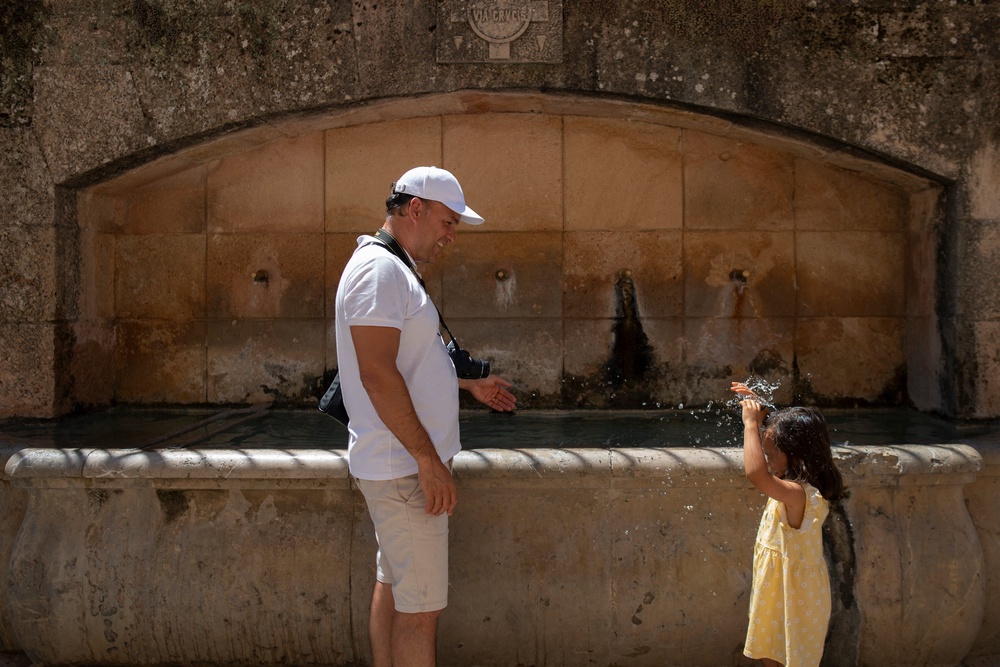 A man cools off with his daughter at a fountain in Ronda, southern Spain. On Reddit threads, Americans rave about living abroad in countries that provide free healthcare, significantly cheaper higher education and access to more affordable everyday needs such as groceries (AFP via Getty Images)
