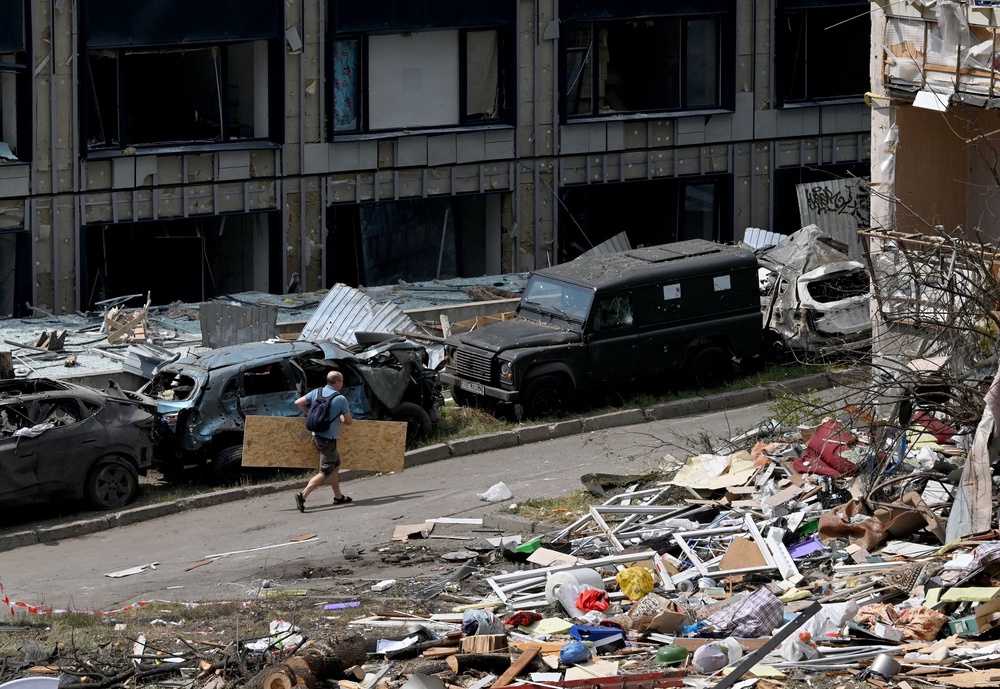 A local resident carries a plywood board past debris and a residential building damaged following a Russian air attack on Kyiv (AFP via Getty Images)
