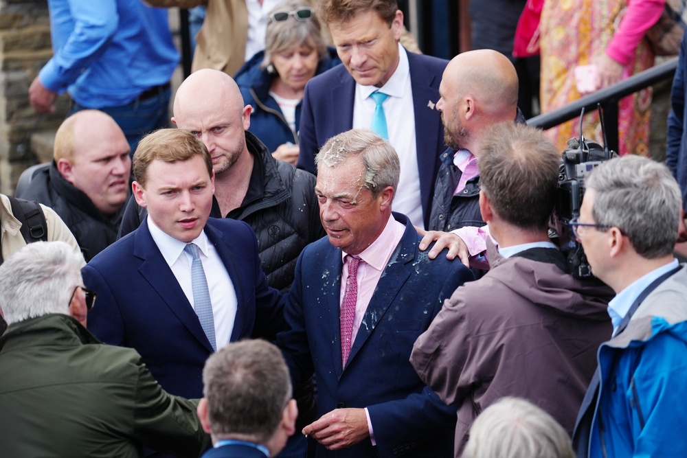 George Cottrell (L) looks on as Reform UK party leader Nigel Farage reacts after a woman threw a drink over him, as he launches his election candidacy at Clacton Pier on June 4, 2024 in Clacton-on-Sea, England. (Getty)
