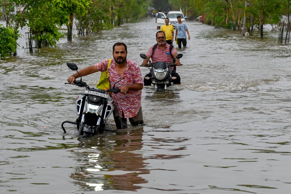 People wade through a flooded street in Vasai on 8 July 2026 (AFP/Getty)