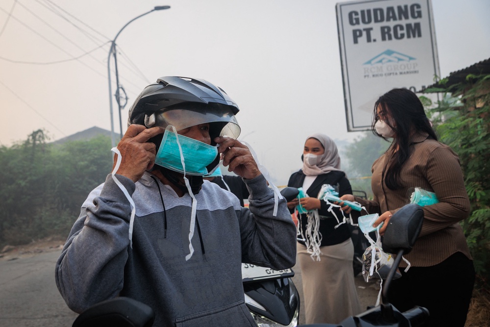A man wears a face mask distributed by volunteers as smoke billows from a fire at the Jatiwaringin landfill (AFP/Getty)