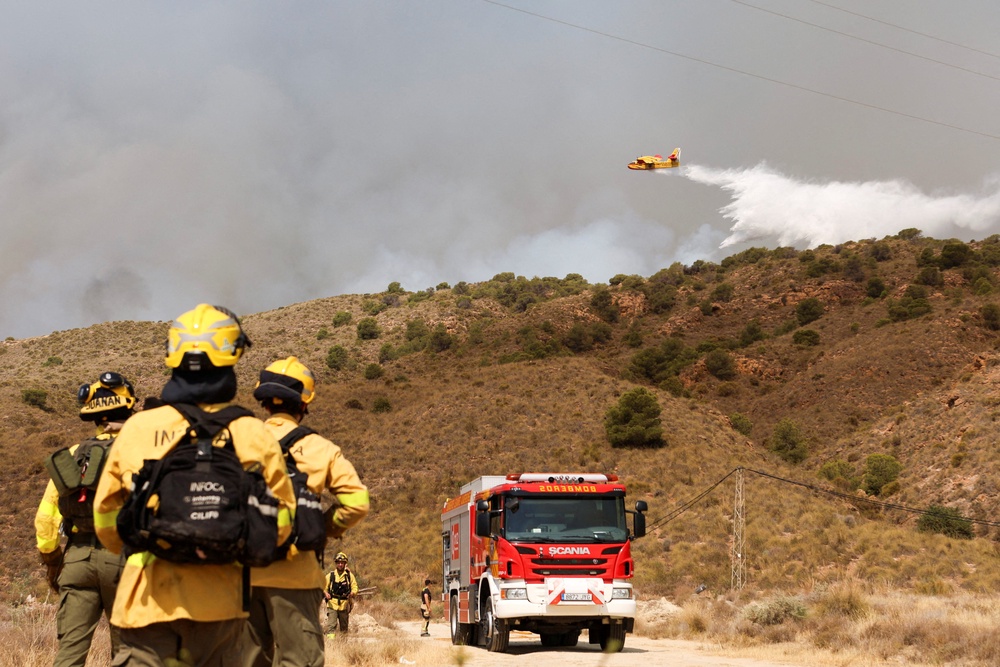 Firefighters look on as water is thrown over a wildfire in Los Gallardos, Almeria, Spain (Reuters)