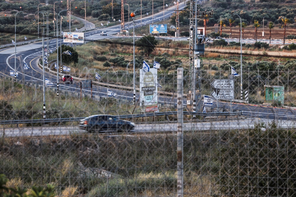 The road between Sinjil and Turmus Ayya, seen through the tall metal fencing installed by the Israeli military that closed off four of the five entrances to Sinjil, near Ramallah, in the Israeli-occupied West Bank, June 26, 2026 (Reuters)