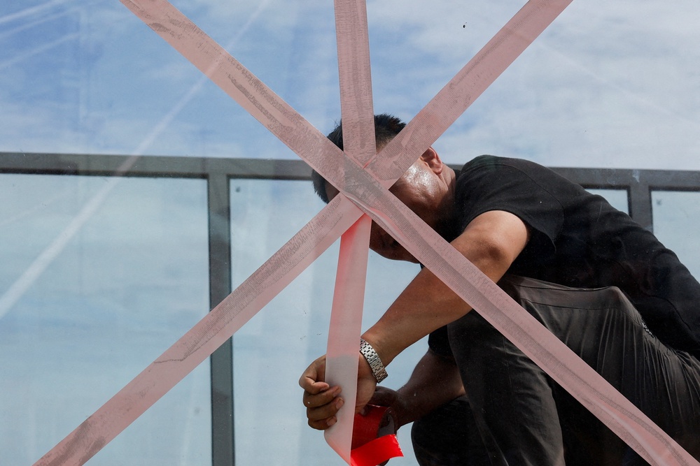 A person applies tape to a glass wall on a pedestrian bridge to secure it as Typhoon Bavi approaches Wenzhou (Reuters)