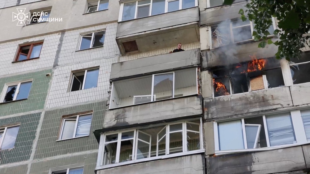 A person looks out from a damaged building, as flames and smoke rise, following a Russian airstrike (Reuters)