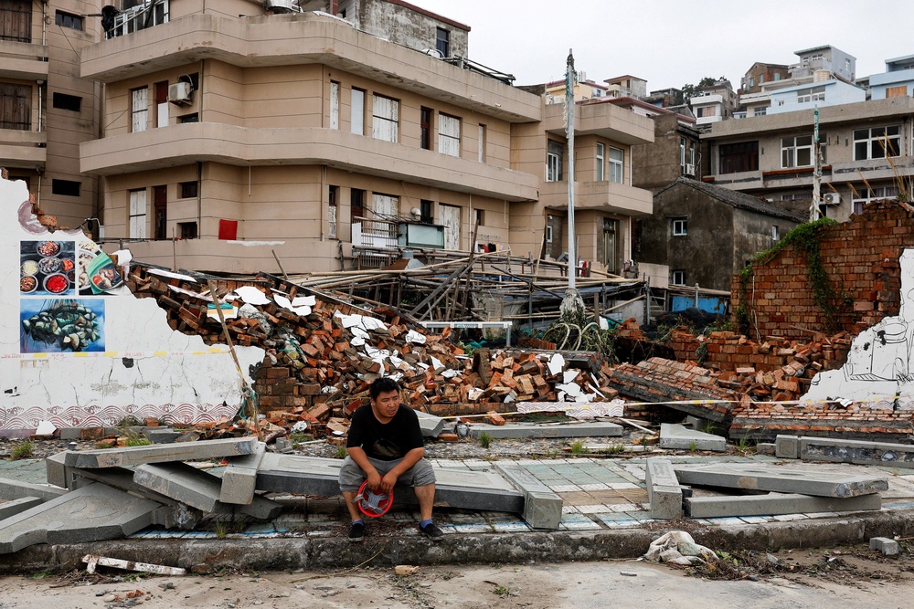 A person sits beside a collapsed wall in the aftermath of Typhoon Bavi in the coastal village of Dongsha, Taizhou, Zhejiang province, China (Reuters)