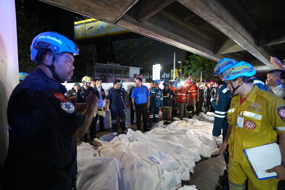 Thailand Prime Minister Anutin Charnvirakul, in blue, inspects the site of a fire as bodies of victims are laid in a row in Bangkok (AP)