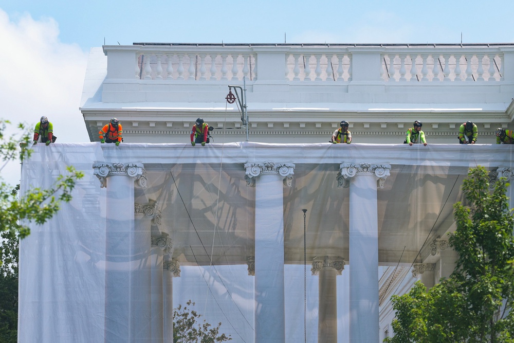 Workers hanging tarp from the White House to conceal the scaffolding that has gone up around its signature columns (Getty)