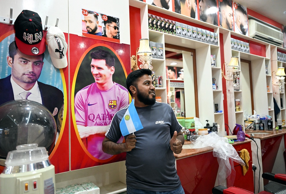 File. A worker of Bangladesh poses with an Argentinian flag in front a photo of Argentina's forward Lionel Messi in a hairdresser shop in Doha on December 6, 2022 (AFP/Getty)