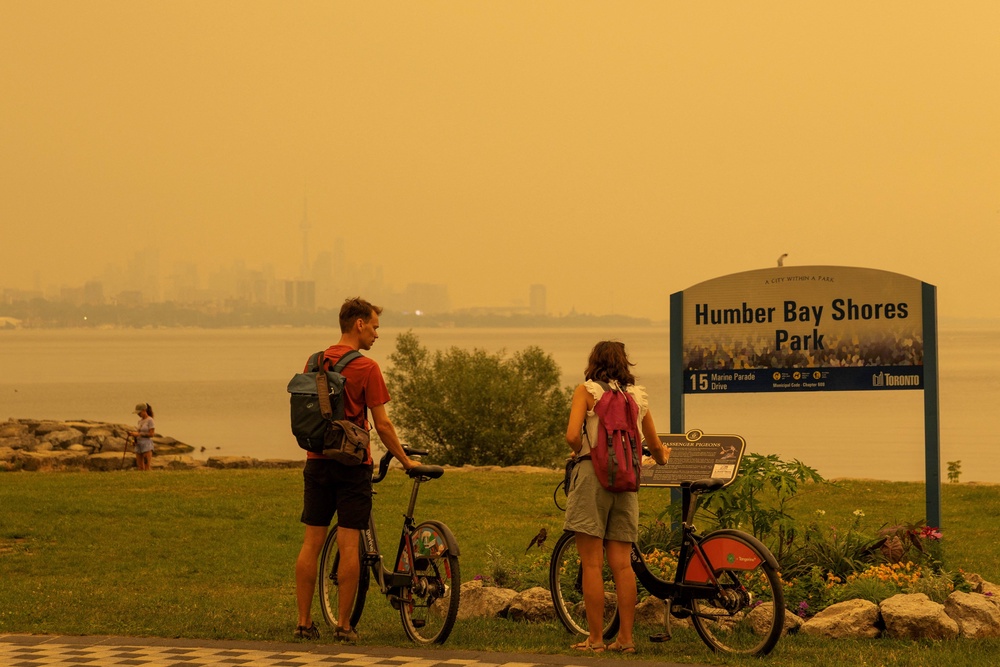 Two people read a sign at a park as wildfire smoke from northwestern Ontario fills the sky in Toronto, Canada, on Wednesday. Hundreds of Canadian wildfires are sending choking smoke across provinces and into the U.S. (REUTERS)