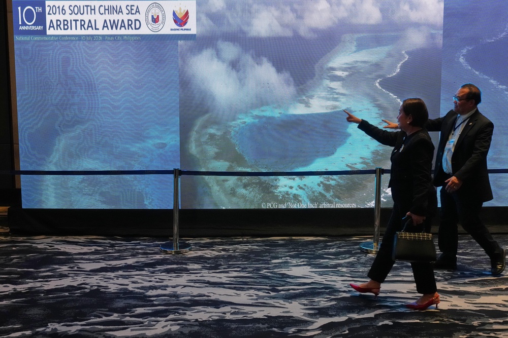 People pass by an electronic board showing areas of the disputed South China Sea (AP)