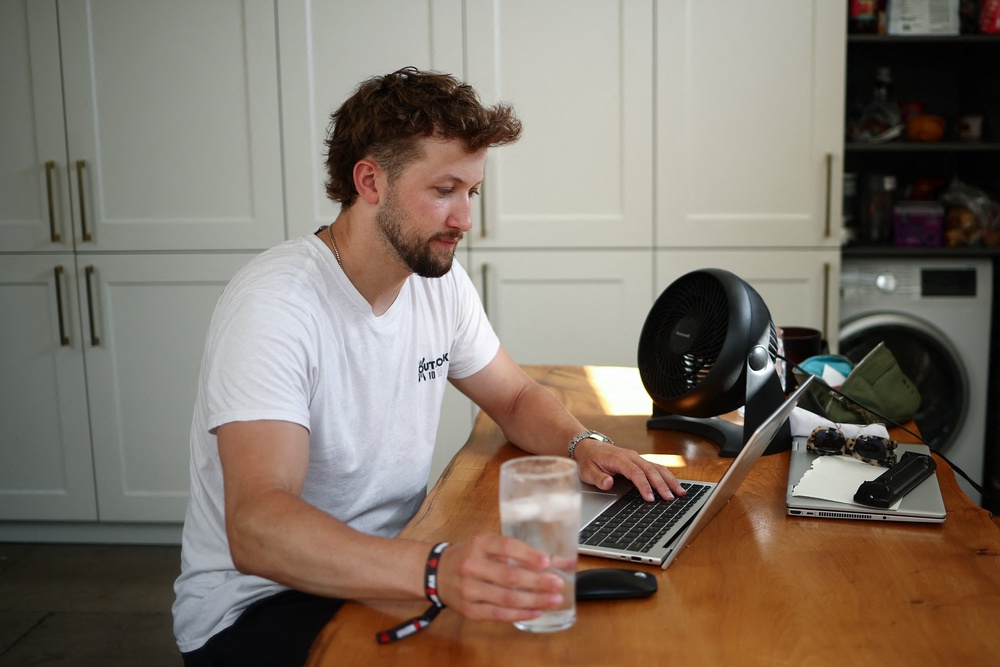 Olly Horrocks, who lives in a Victorian house with no air conditioning, sits next to a fan while working from home (Reuters)