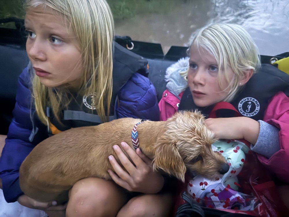 Ella and Grace Sanford and their dog Benjamin ride on a Texas Game Wardens rescue boat after being evacuated from their home after flooding in Uvalde, Texas, on Thursday (AP)