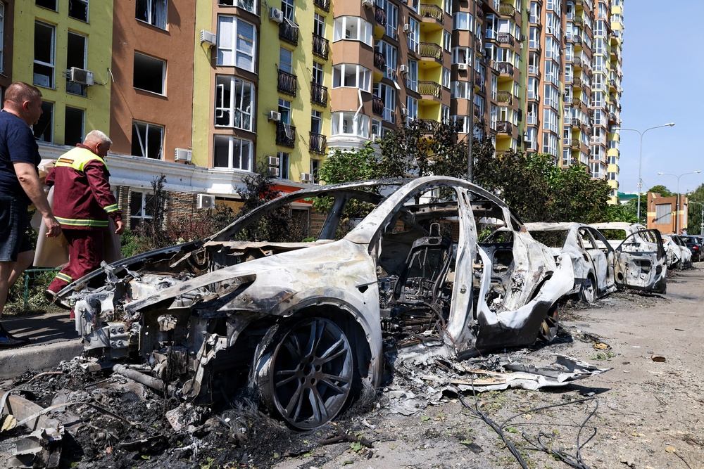 People walk past damaged cars parked in a street following missile strikes in Kyiv (AFP/Getty)