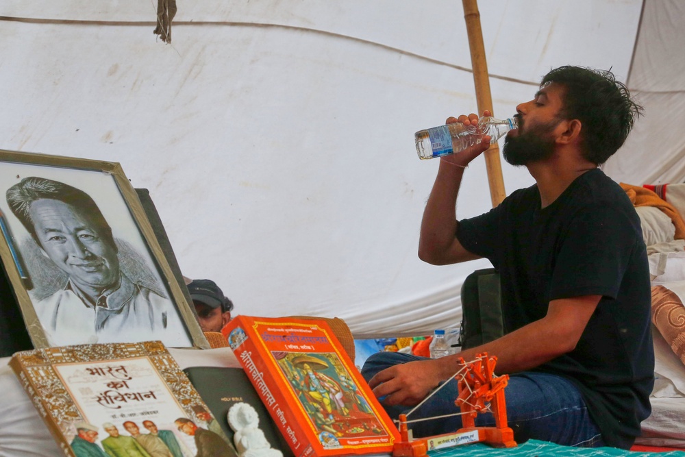 Abhijeet Dipke, founder of the Cockroach Janta Party, sits by a portrait of hunger-striking activist Sonam Wangchuk during a protest in Delhi (AP)