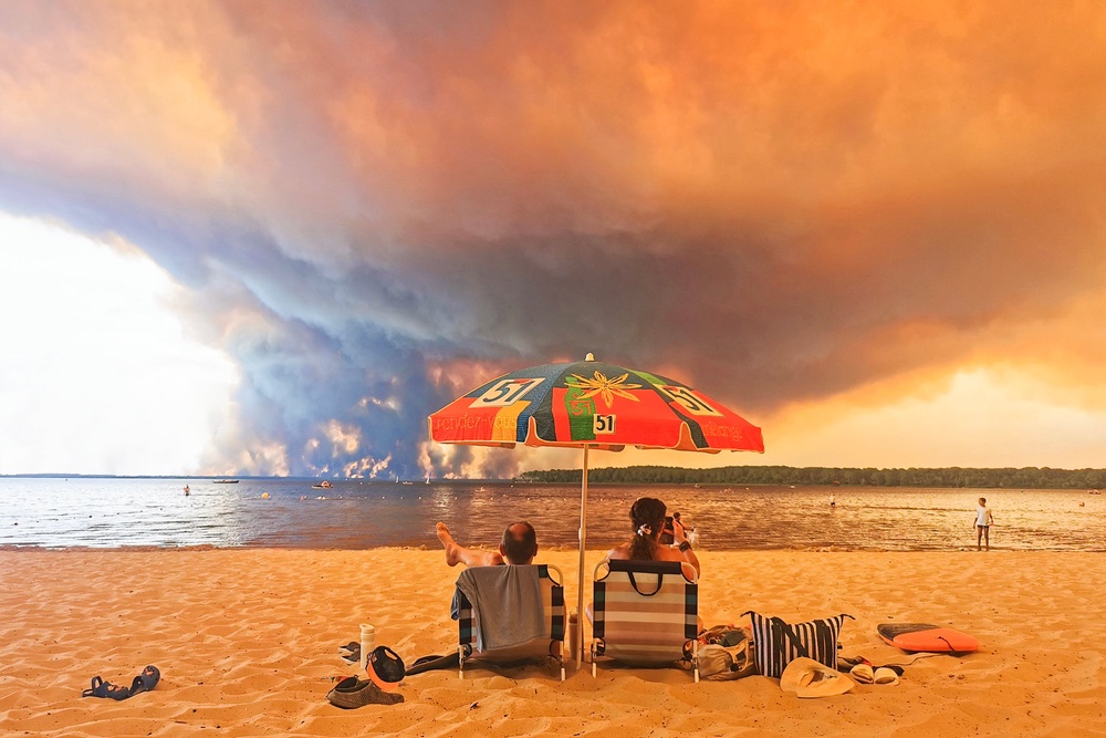 Beach goers sit on the beach of Moutchic in Lacanau, southwestern France on July 24, 2026, as clouds of smoke rise into the sky from a wildfire. (AFP/Getty)