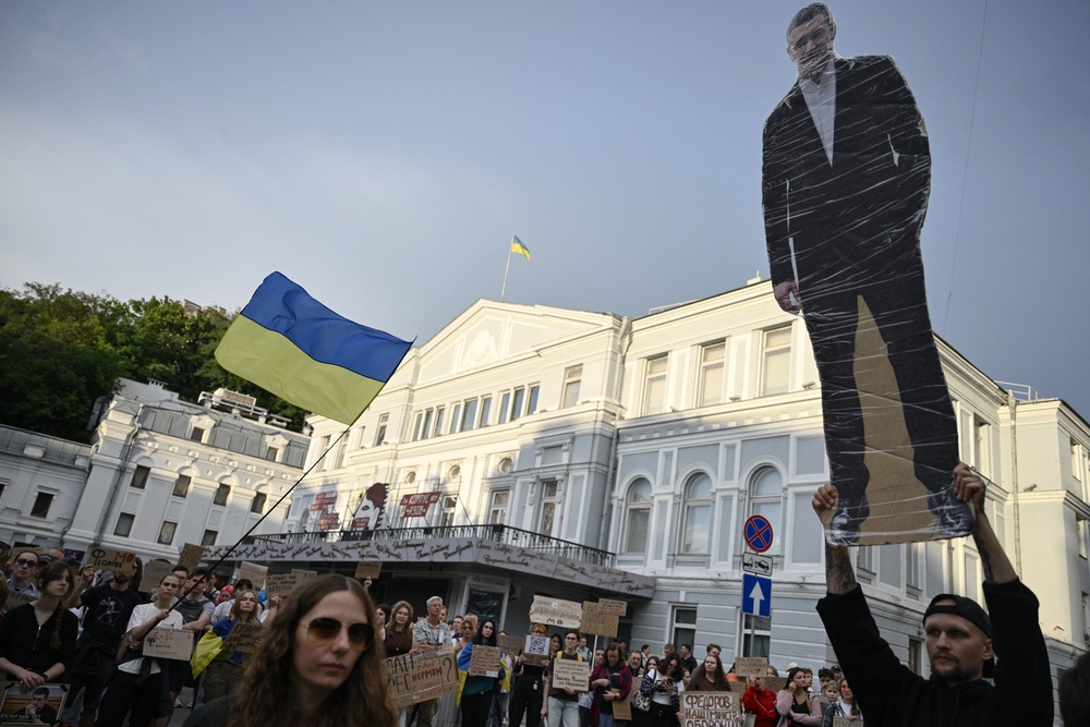 A man (R) holds a portrait placard of former defence minister Mykhailo Fedorov as people take part in a demonstration against Ukraine's President's decision in Kyiv on July 24, 2026, amid the Russian invasion of Ukraine. (AFP/Getty)