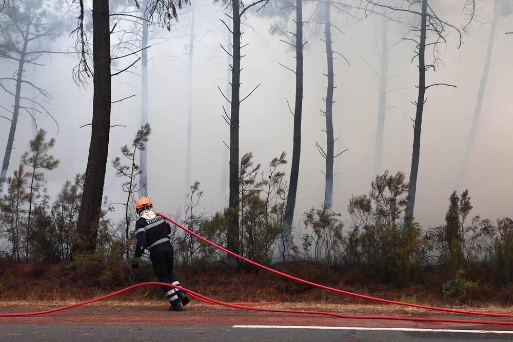 A firefighter from Marseille pulls a hose amid smoke in Ares on July 26, 2026 as a wildfire has been ravaging the forest north of the Arcachon Basin (Gironde) since July 22. The fire that has engulfed the area around the Arcachon Basin and is now threatening the outskirts of the Bordeaux metropolitan area has destroyed 42,000 hectares of 