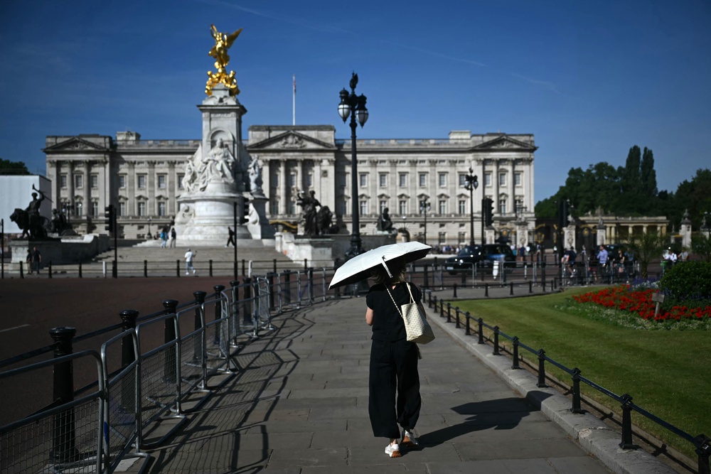 A person uses a parasol umbrella to shelter from the heat of the sun during a heatwave, as they walk near Buckingham Palace (AFP/Getty)