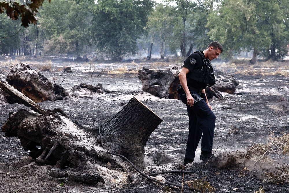 A gendarme covers a small hot spot with soil to prevent any risk of reignition during a patrol, as wildfires rage across the Gironde region amid worsening drought conditions following a heatwave and water shortages across much of the country, in Le Porge, France (Reuters)