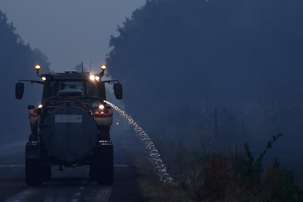 An agricultural worker drives a tractor while wetting roadside vegetation as a preventive measure to help stop wildfires from spreading, as wildfires rage across the Gironde region amid worsening drought conditions following a heatwave and water shortages across much of France, near Sainte-Helene, France (Reuters)