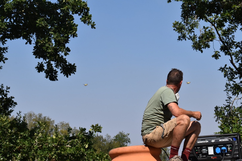A volunteer on top of a truck watches as Canadair water bombers pass overhead (James Reynolds/The Independent)