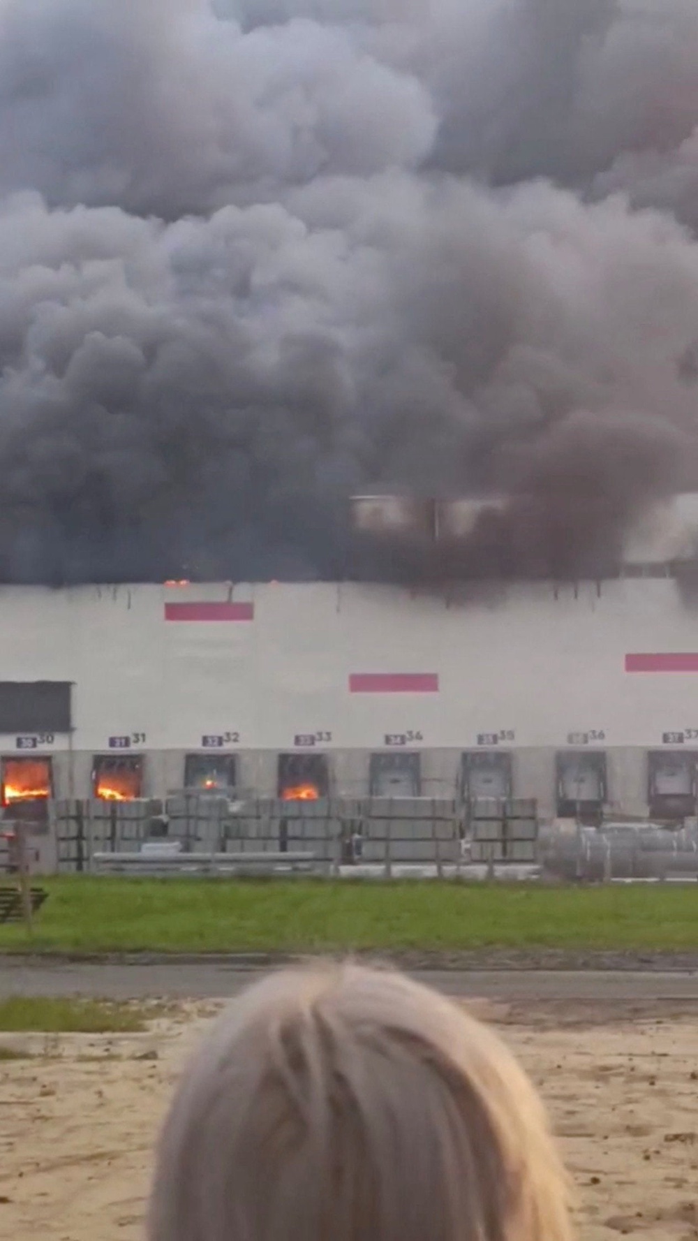 A woman looks on as smoke billows from a Wildberries warehouse after a fire broke out at the facility, in Ryazan region, Russia, 29 July 2026 (Reuters)