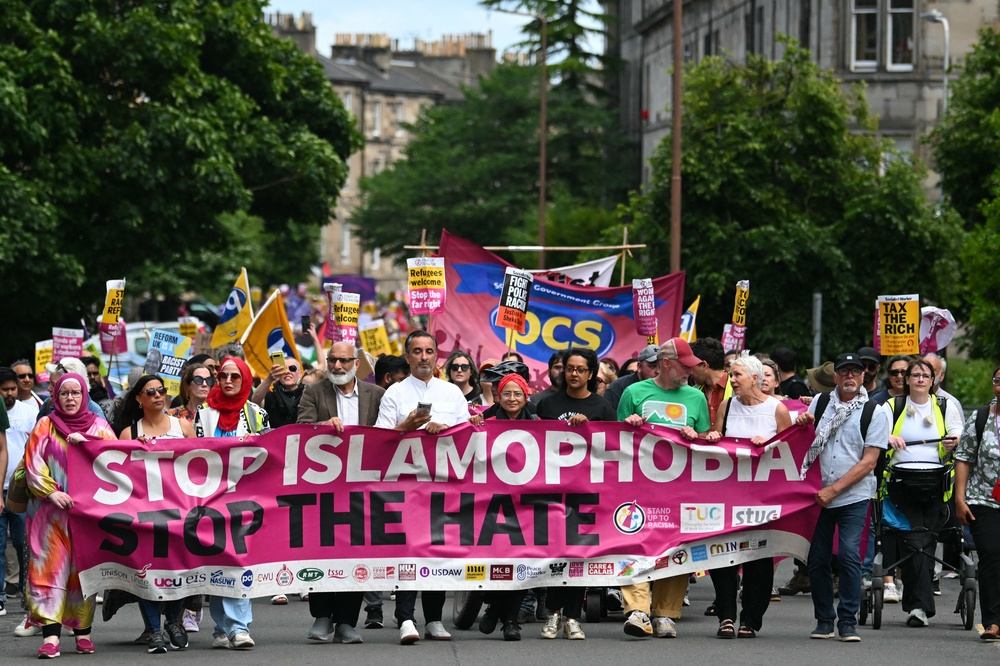 Aamer Anwar (C) and protesters display a banner as they take part in an anti-racism 