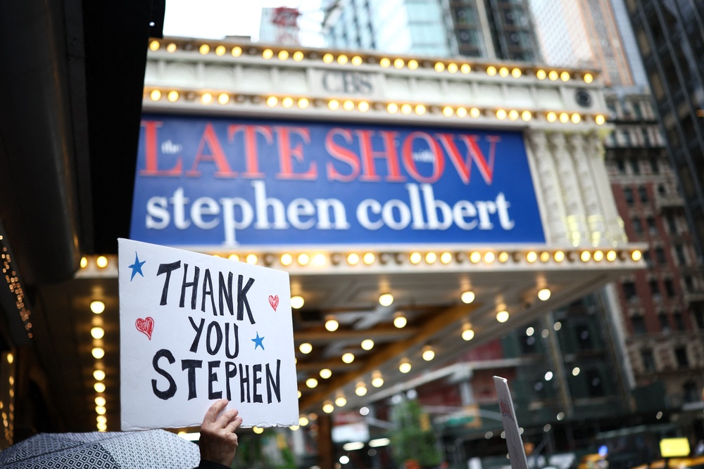 People hold signs supporting Stephen Colbert outside the Ed Sullivan Theater ahead of the taping of the final episode of the The Late Show on May 21, 2026 (AFP via Getty Images)