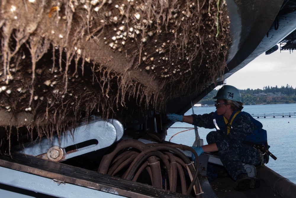 Sailor scrapes barnacles from the bottom of a rigid-hull inflatable boat (US Navy/Christopher Frost)